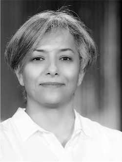 Black and white portrait of Amani Albedah, looking directly at the camera with a gentle smile. She is wearing a white shirt, and the background is softly blurred.